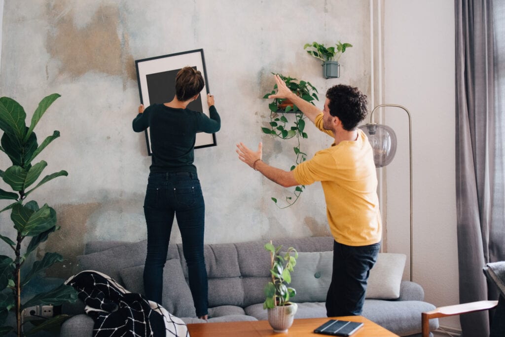 People styling a room and adjusting a framed artwork